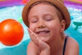 Young girl playing in colorful rainbow inflatable water swimming pool with orange ball. Happy child in straw hat smiling