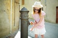 Young girl playing with drinking water fountain in Montalcino town, located on top of a hill top and surrounded by vineyards,