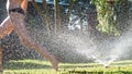 Young girl playing jumping in a garden water lawn sprinkler