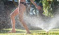 Young girl playing jumping in a garden water lawn sprinkler