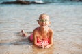 Young girl playing, swiming and splashing in fresh sea water. Smilling blonde girl in swimsuit with and swimming goggles Royalty Free Stock Photo