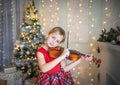 Young girl playing violin in front of christmas tree. Royalty Free Stock Photo