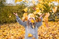 Young girl is playing with yellow fallen leaves and smiling. Child is throwing maple leaves up in autumn park. Royalty Free Stock Photo