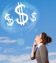 Young girl pointing at dollar sign clouds on blue sky Royalty Free Stock Photo