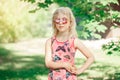 Young girl posing in fancy pink pentagonal shaped sunglasses outdoors. Cute serious pensive stylish Caucasian child with long