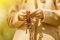 Young girl praying with wooden rosary. Close up