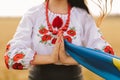 Young girl prays in the wheat field wearing Ukrainian national embroidered shirt with flower red wreath and holds flag at sunset y Royalty Free Stock Photo