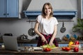 Young girl prepares a vegetarian salad in the kitchen and looks into a laptop, she learns to cook by a video tutorial, preparing Royalty Free Stock Photo