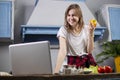 Young girl prepares a vegetarian salad in the kitchen and looks into a laptop, she learns to cook by a video tutorial, preparing Royalty Free Stock Photo