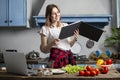 Young girl prepares a vegetarian salad in the kitchen and looks into a recipe book, she learn to cook and reads Royalty Free Stock Photo