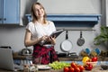 Young girl prepares a vegetarian salad in the kitchen and looks into a recipe book, she learn to cook and reads Royalty Free Stock Photo