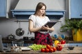 Young girl prepares a vegetarian salad in the kitchen and looks into a recipe book, she learn to cook and reads Royalty Free Stock Photo