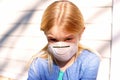 Young girl with protective anti viral face mask sits outdoors.