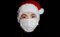 A young girl in a protective mask in a Santa Claus hat. Portrait of a brunette girl on a black background Royalty Free Stock Photo