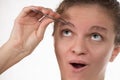 Young girl pulls out her eyebrows with tweezers metal on a white Royalty Free Stock Photo