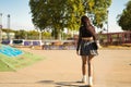 Young girl with punk style holding a skateboard with her hand walking backwards in a skateboard park Royalty Free Stock Photo