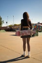 Young girl with punk style holding a skateboard with her hands behind her back in a skateboard park