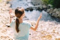 Young girl raises her arms praying on the banks of a mountain stream