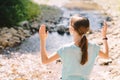 Young girl raises her arms praying on the banks of a mountain stream