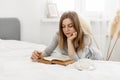 Young girl reading a book and daydreaming while sitting on the bed at home Royalty Free Stock Photo