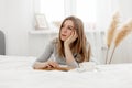 Young girl reading a book and daydreaming while sitting on the bed at home Royalty Free Stock Photo