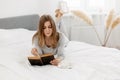 Young girl reading a book and daydreaming while sitting on the bed at home Royalty Free Stock Photo