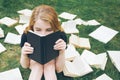 Young girl reading a book while lying in the grass. A girl among the books in the summer garden Royalty Free Stock Photo