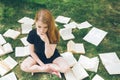 Young girl reading a book while lying in the grass. A girl among the books in the summer garden Royalty Free Stock Photo