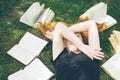 Young girl reading a book while lying in the grass. A girl among the books in the summer garden Royalty Free Stock Photo