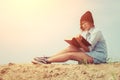 Young girl reading book and sitting on the beach with sunrise Royalty Free Stock Photo