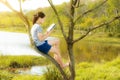 Young girl reading a book on the tree in gold river contryside n Royalty Free Stock Photo