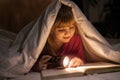 A young girl reading a book under the covers with a flashlight Royalty Free Stock Photo