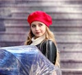 Girl in a red biret and with an umbrella and a black jacket stands walking near the Eiffel Tower