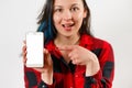 A young girl in a red and black shirt holds a smartphone with an empty white screen vertically in front of her, points at it with Royalty Free Stock Photo