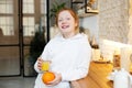 Young girl with red curly hair drinks orange juice standing in the kitchen, healthy food for baby Royalty Free Stock Photo