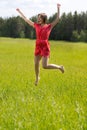 Young girl in a red dress jumping in a field Royalty Free Stock Photo