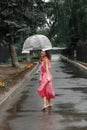 Young girl in a red dress with a transparent umbrella dancing in the rain standing in a puddle Royalty Free Stock Photo