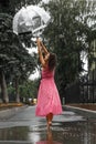Young girl in a red dress with a transparent umbrella dancing in the rain standing in a puddle Royalty Free Stock Photo