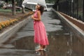 Young girl in a red dress with a transparent umbrella dancing in the rain standing in a puddle Royalty Free Stock Photo