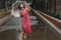 Young girl in a red dress with a transparent umbrella dancing in the rain standing in a puddle Royalty Free Stock Photo