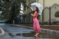 Young girl in a red dress with a transparent umbrella dancing in the rain standing in a puddle Royalty Free Stock Photo