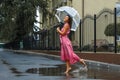 Young girl in a red dress with a transparent umbrella dancing in the rain standing in a puddle Royalty Free Stock Photo