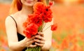 A young girl with red hair in a black sundress holds a bouquet with poppies in a poppy field outside the city. Summer and
