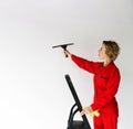 a young girl in a red jumpsuit, an employee of a cleaning company, stands on a stepladder and holds a glass scraper in Royalty Free Stock Photo