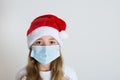 Young girl with red santa claus hat and mask isolated on white background. Sad child face with surgical mask. Christmas covid 19 Royalty Free Stock Photo