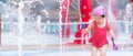 Young girl in red swimming suits and pink hats play in the fountain courtyard rising from water park area, running is funny. Royalty Free Stock Photo