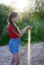 young girl in red T-shirt and denim shorts holds sand in her palms. The sand sifts through my fingers