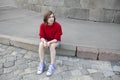 Young girl in a red wool sweater and jeans shorts is sitting on the steps Royalty Free Stock Photo