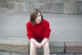 Young girl in a red wool sweater and jeans shorts is sitting on the steps Royalty Free Stock Photo