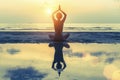 Young girl (with reflection in the water) practicing yoga on the beach during sunset. Royalty Free Stock Photo